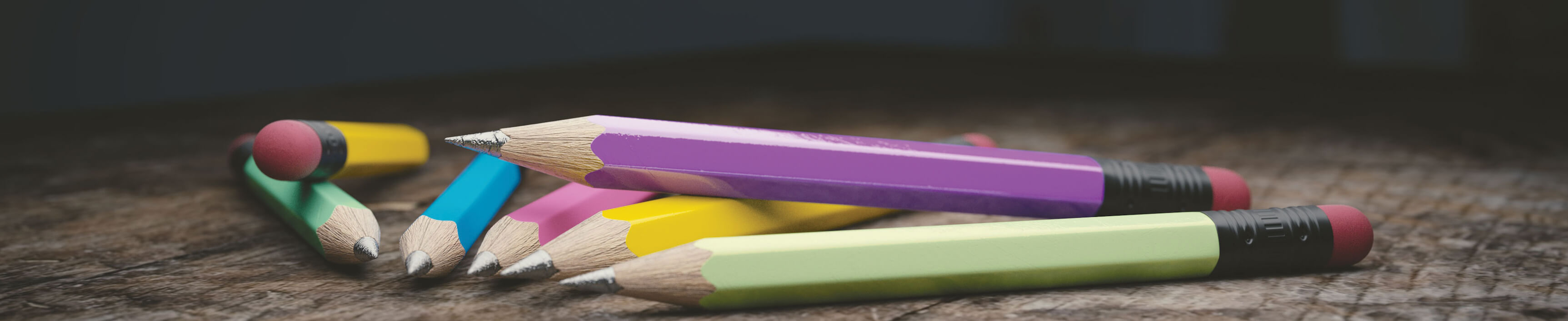 Siete lápices de madera de diferentes colores sobre un piso de madera
